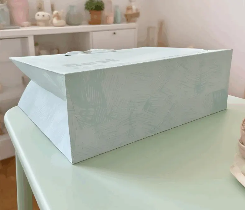 This handbag is named FH-22019-L Cross-border Wholesale Simple Cardstock Gift Bag with Good Wishes. It is made of high-quality cardstock material, which is crisp and well-shaped, and can firmly hold items. The surface is printed with fine techniques, with a light blue tone that is fresh and elegant. Paired with simple text patterns, it is simple yet stylish. The white handle design is in harmony with the color of the bag body and is also sturdy and durable. It is suitable for carrying goods and gift packaging when shopping, or for daily storage and carrying small items, etc. Whether it is for shopping or gift-giving occasions, it can show elegant taste.Product uses: Packaging paper bags, shopping paper bags, gift paper bags, festival paper bags, promotional paper bags.